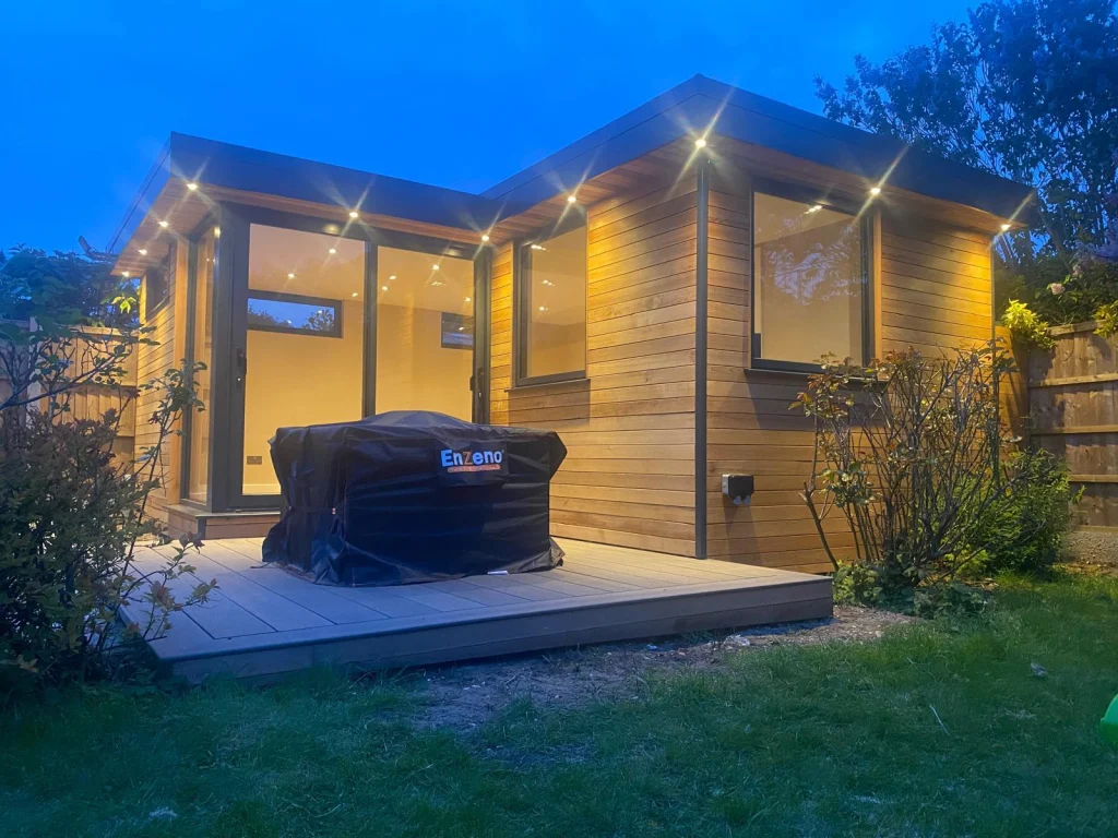Cedar garden room lit up at dusk beside a seating area